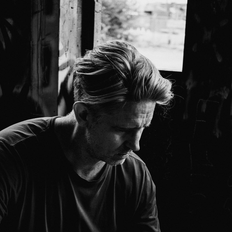 Josh Tyson, in black and white, looking down beside a bright window